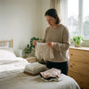 Volwassene in een rustige slaapkamer bekijkt zacht katoenen ondergoed, met focus op comfort, huidvriendelijke stoffen en een ontspannen ochtendmoment.
