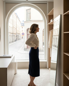 Vrouw in lichte blouse en rok past corrigerend ondergoed in een rustige kleedkamer met zacht daglicht en een verzorgde, comfortabele sfeer.