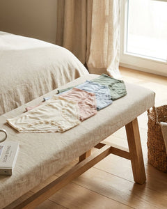 Neatly folded women’s hipster briefs in soft neutral tones on a bright bedroom bench, styled with cotton fabric textures and a calm, premium feel.
