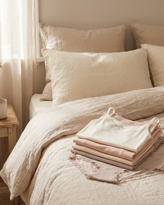 Soft neutral bedroom scene with folded Sloggi Romance slips and tops featuring delicate lace trim on a bed, lit by gentle morning daylight.