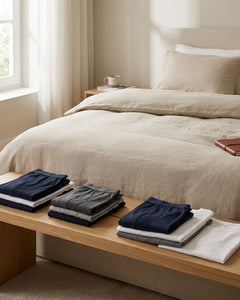 Folded Schiesser Long Life underwear and soft basics on a neatly made bed in a bright Belgian bedroom, conveying everyday comfort and lasting quality.