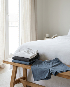 Neatly folded Schiesser men’s boxershorts in fitted and loose styles on a clean bedroom bench with soft daylight and a calm Belgian home feel.